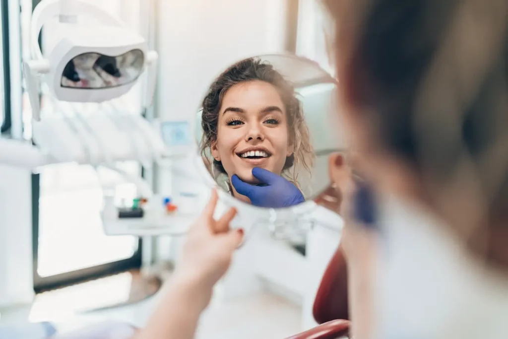 kobieta u dentysty patrzy w lusterku na swoje zęby