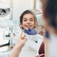 kobieta u dentysty patrzy w lusterku na swoje zęby
